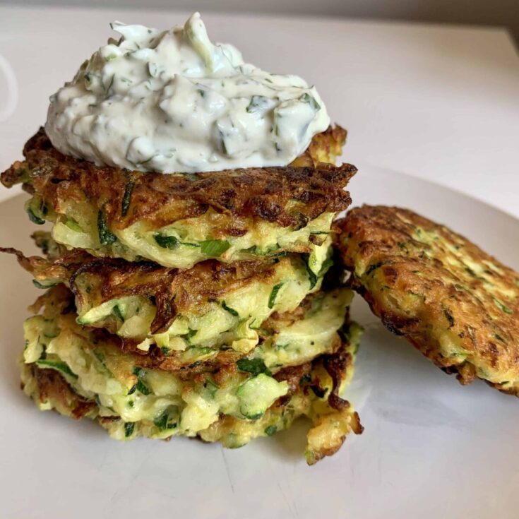 Golden brown zucchini fritters in a stack with a dollop of herbed yogurt on top.