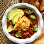 Bowl of basic instant pot chili topped with cheese, corn chips, avocado and cilantro