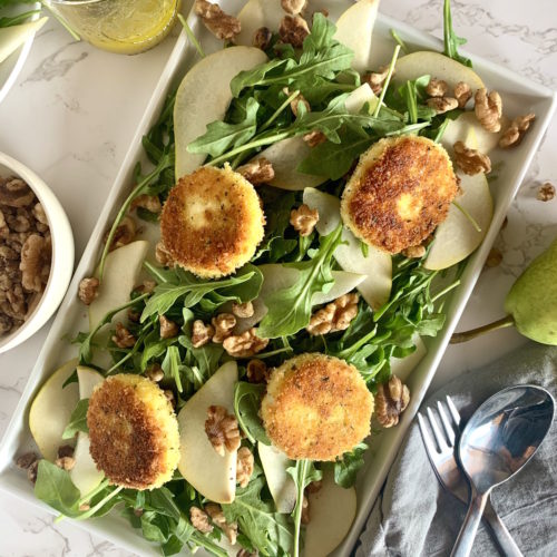 Rounds of fried goat cheese on a bed of arugula with walnuts and pears on a platter