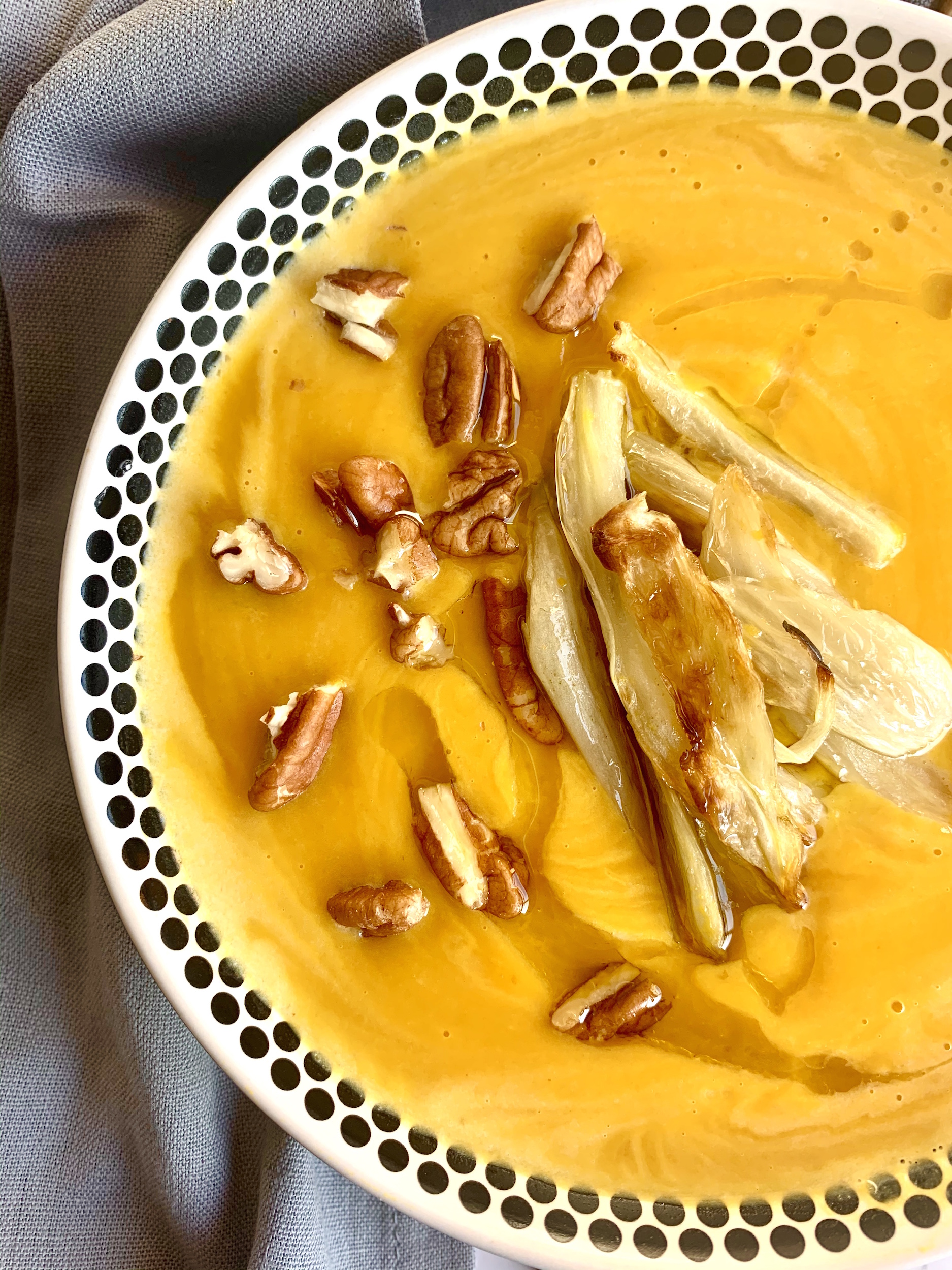 Close up of bowl of red kuri squash soup topped with pecans, olive oil and roasted fennel