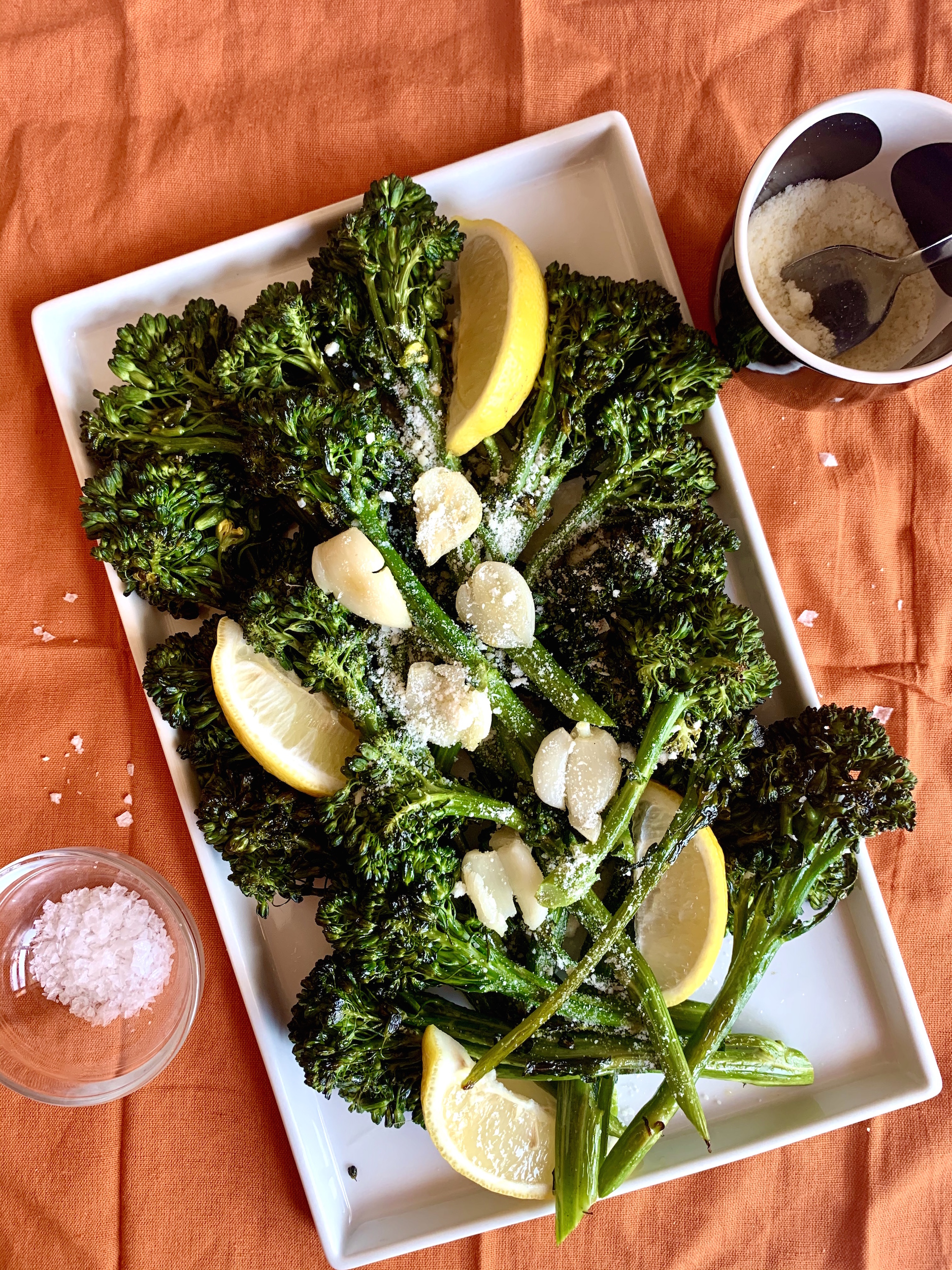 Roasted broccolini on a platter with garlic, lemon wedges and parmesan cheese.
