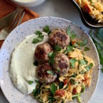 Speckled plate with whipped feta, greek meatballs on a bed of orzo, sprinkled with fresh herbs.
