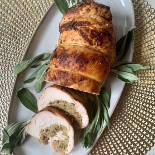 Gold placemat with grey platter of turkey roulade with stuffing and fresh sage leaves for garnish