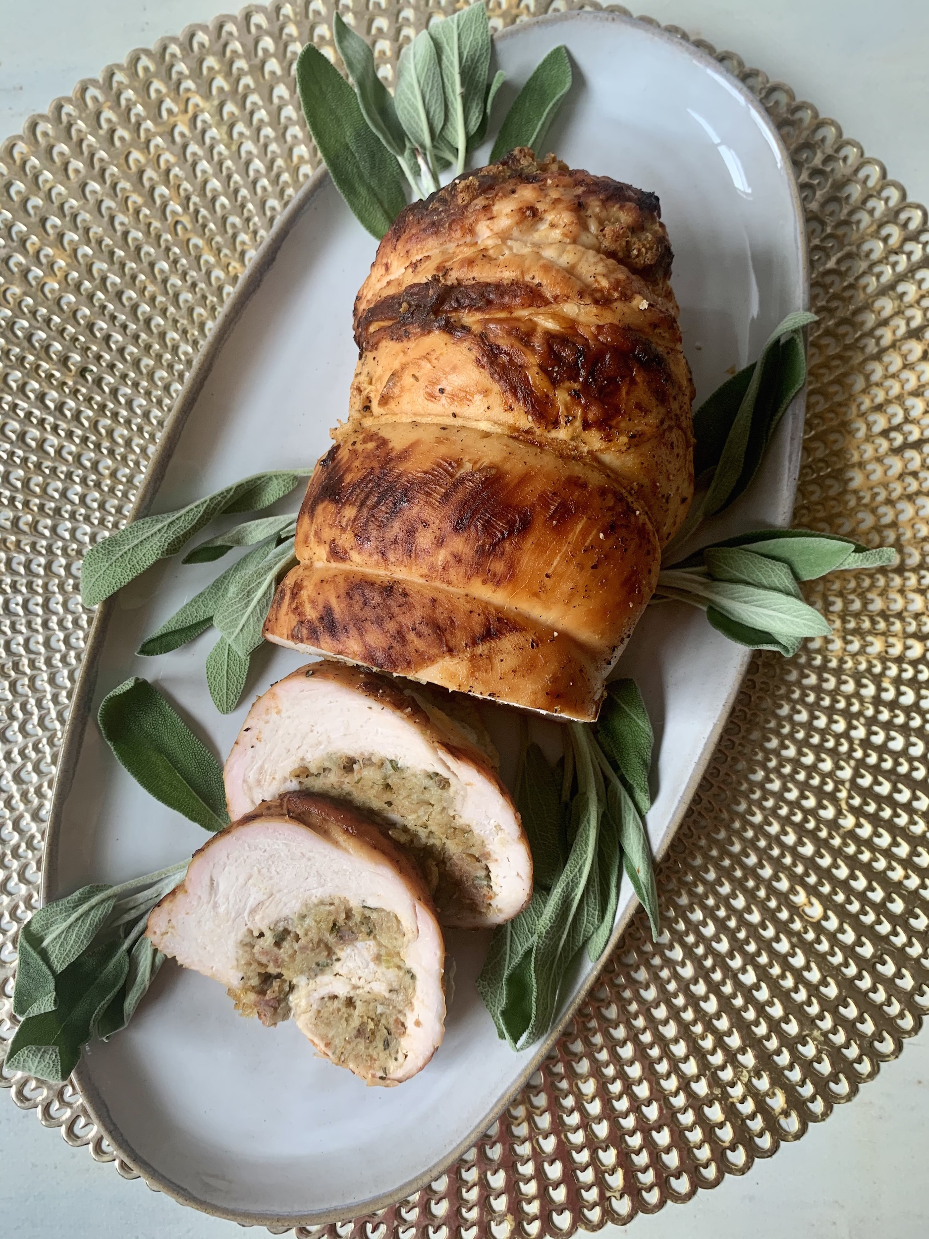 Gold placemat with grey platter of turkey roulade with stuffing and fresh sage leaves for garnish