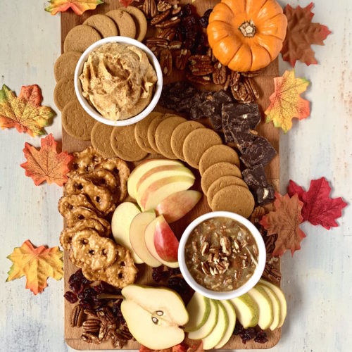 Board with Pumpkin pie dip, caramel pecan dip, fruit, cookies and nuts with a pumpkin and leaves decoration.