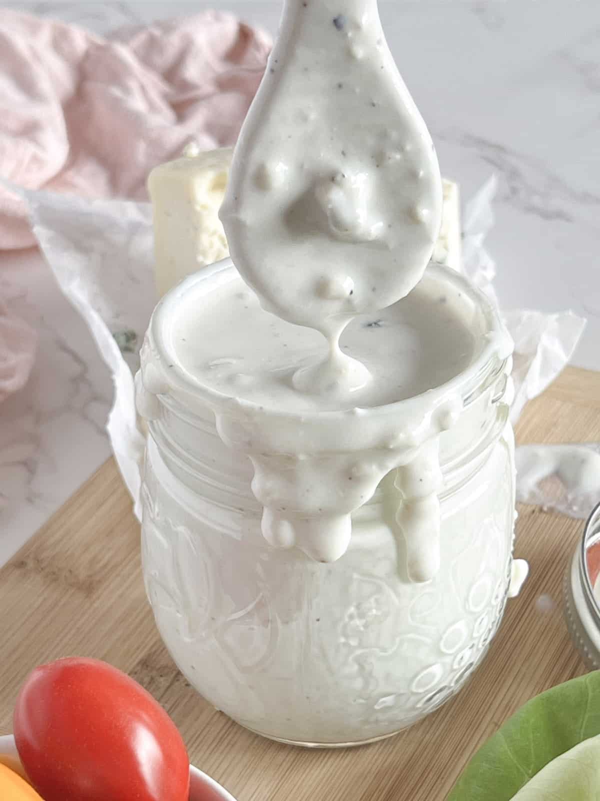Small mason jar of blue cheese dressing with drips over the side and a drizzling spoon.