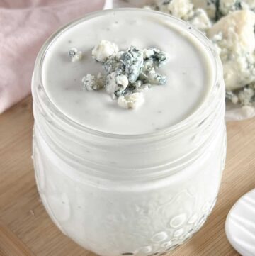 Small mason jar full of blue cheese dressing topped with crumbled cheese.