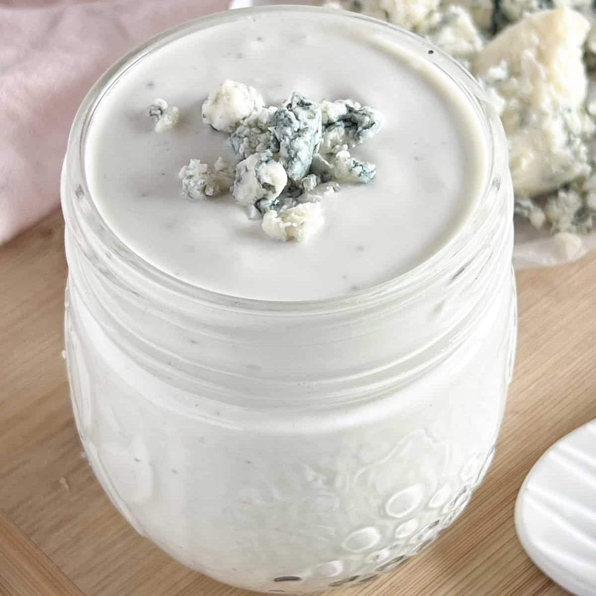 Small mason jar full of blue cheese dressing topped with crumbled cheese.