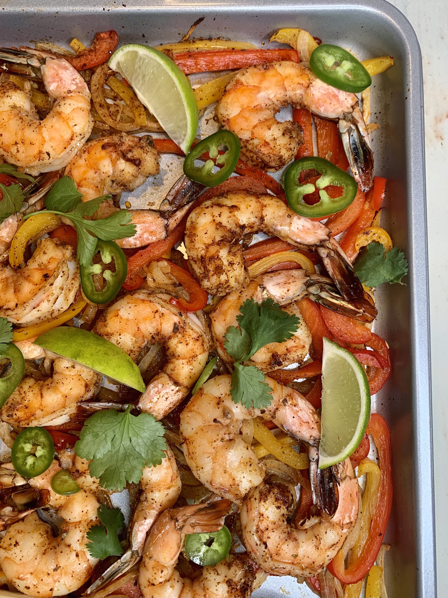 upper right hand corner view of sheet pan with shrimp, onions, peppers, cilantro, jalapeno and lime