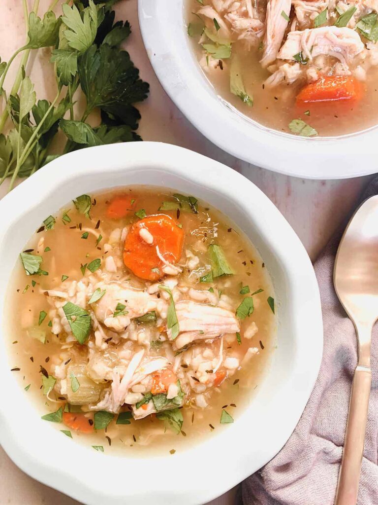 Light blue bowl of Instant Pot Chicken and brown rice soup with a gold spoon and fresh parsley in the background.