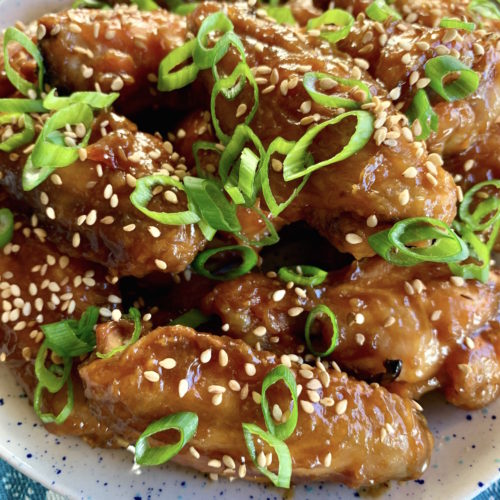 Close up of asian style chicken wings on a white plate on a blue printed cloth.