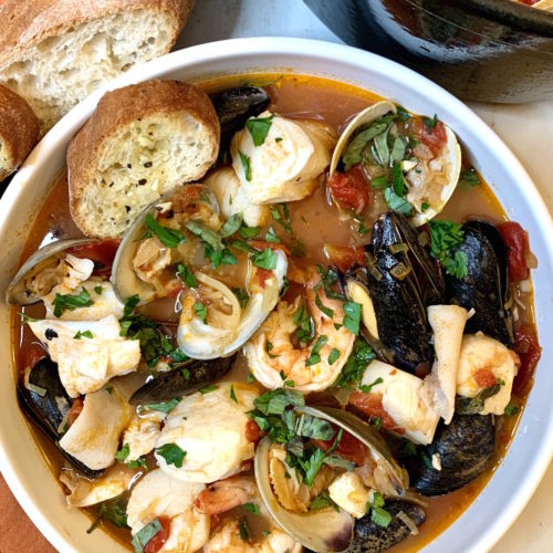 White bowl full of cioppino with crusty bread and black dutch oven in the background