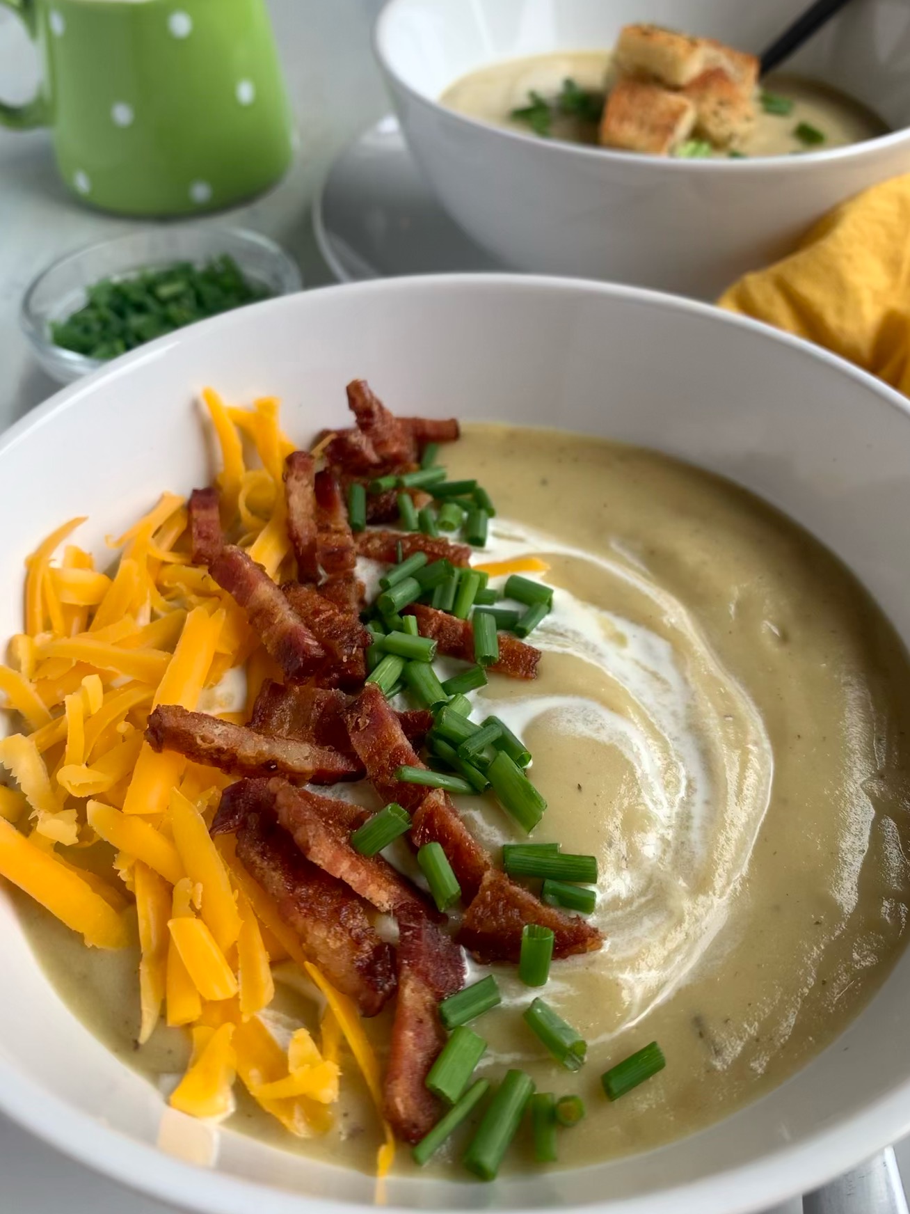 Close up of creamy potato, leek and cauliflower soup with bacon, cheddar, chives and a swirl of cream