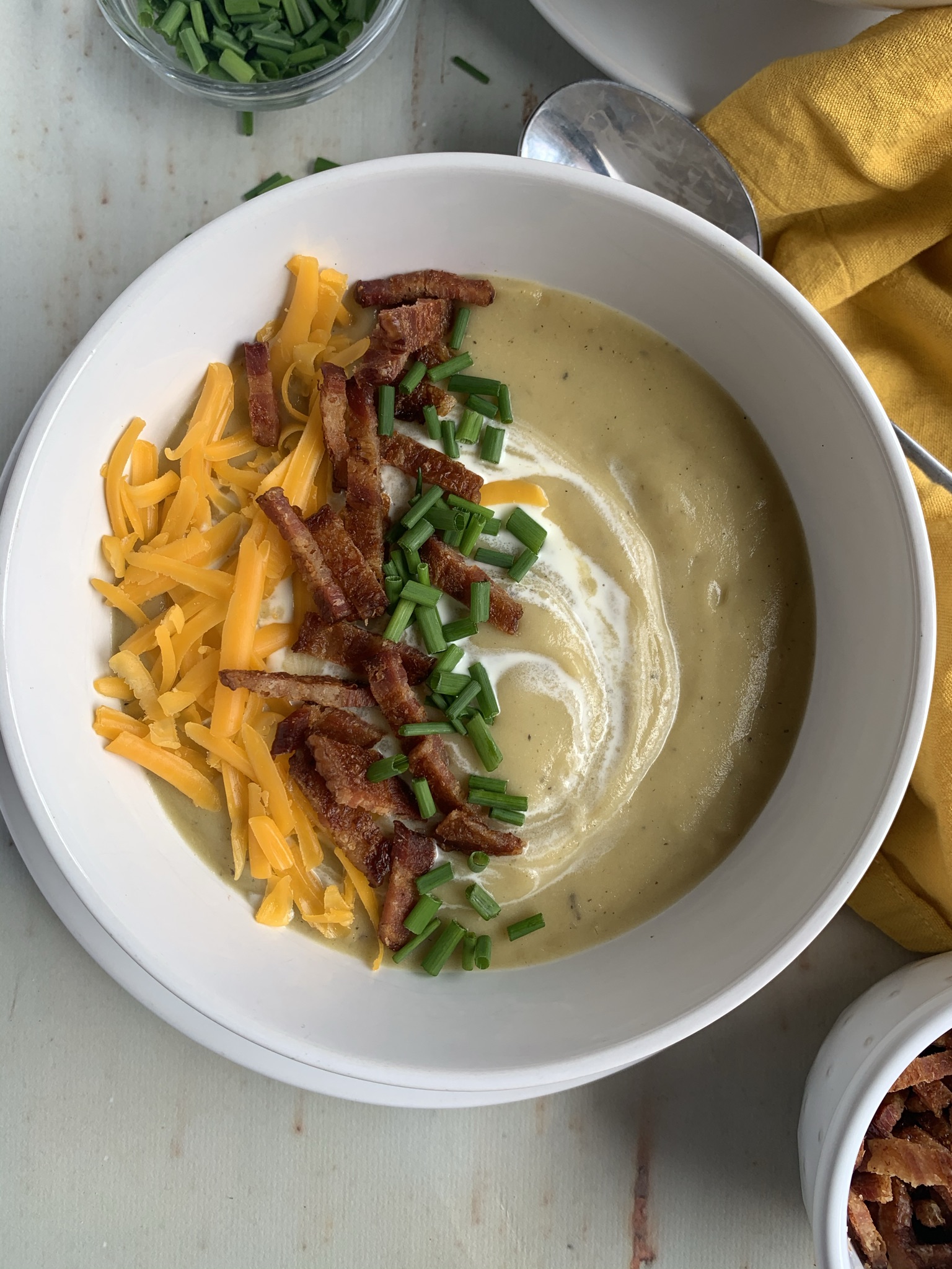 Bowl of creamy potato, cauliflower and leek soup topped with cheddar, bacon and chives and a swirl of cream