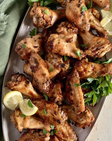 Grey platter with baked peri peri chicken wings, garnished with parsley and lemon with a green linen napkin