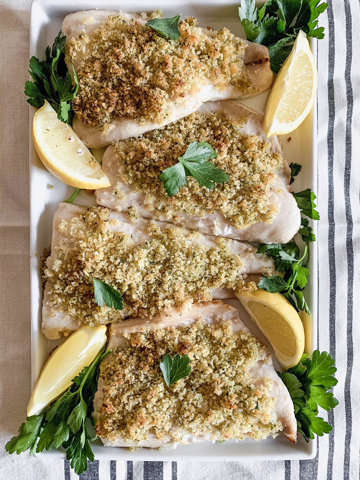 A platter of baked Panko-crusted whitefish on a striped tablecloth.