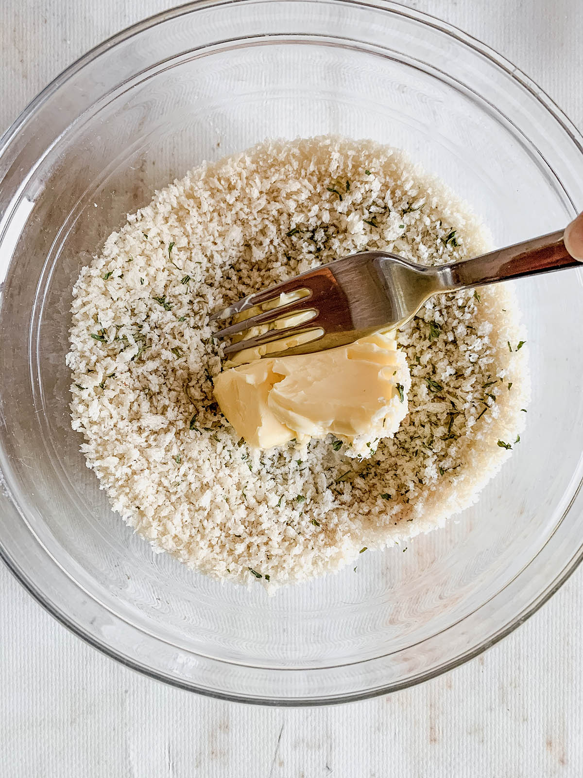 Panko breadcrumbs and spices mixed in a bowl with a chunk of butter on top and a fork about to mix the butter in.