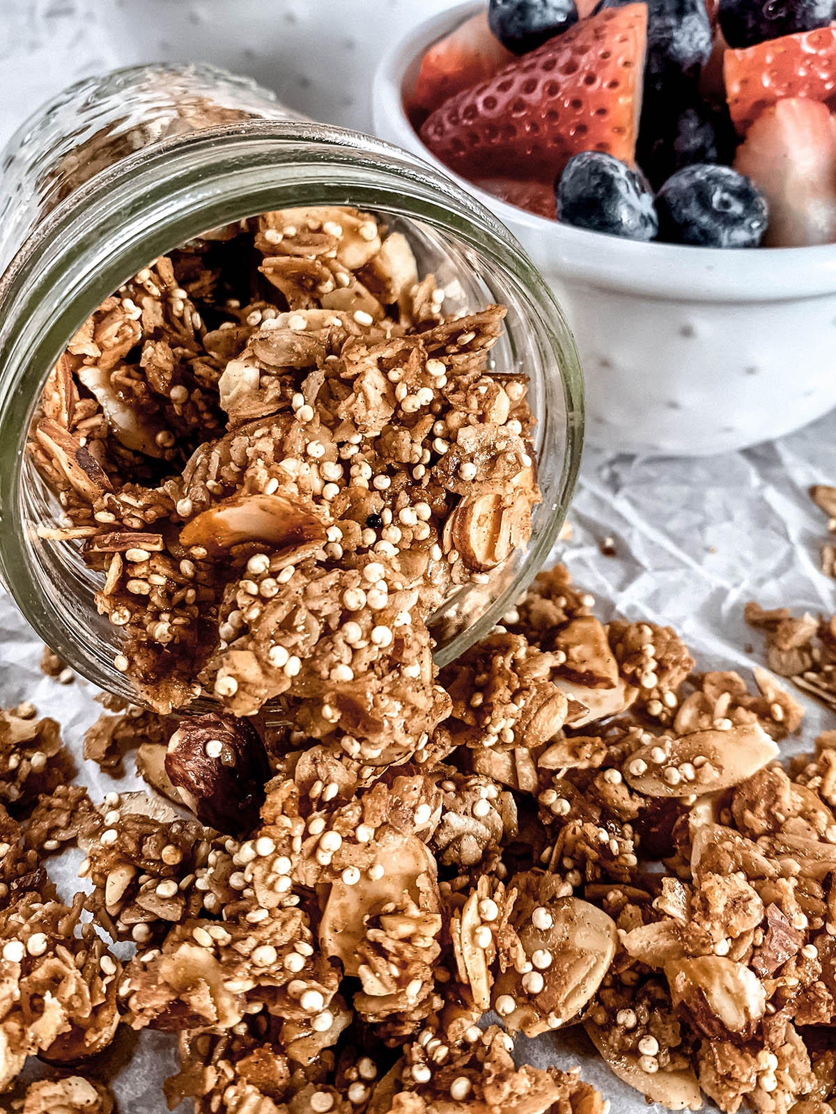 Granola spilling out of mason jar with berries in the background.