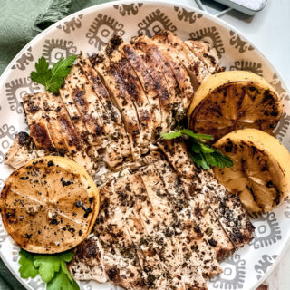 Grilled Mediterranean Chicken in a white patterned bowl with charred lemon and parsley