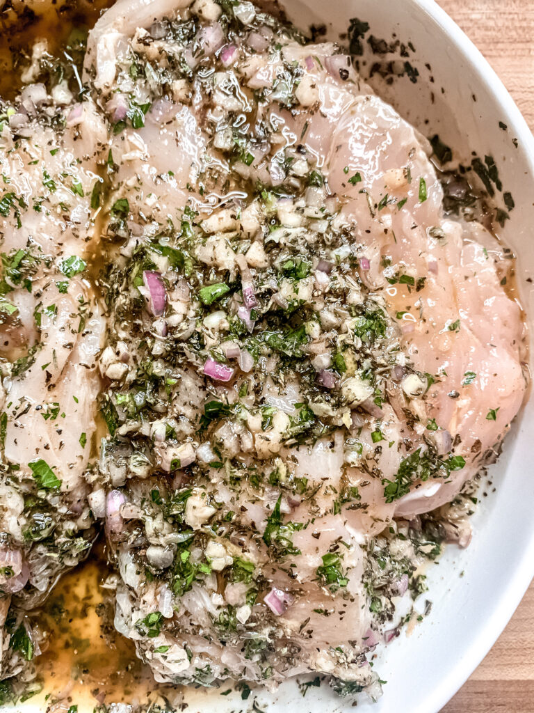 Raw chicken breasts in a shallow white bowl covered in marinade