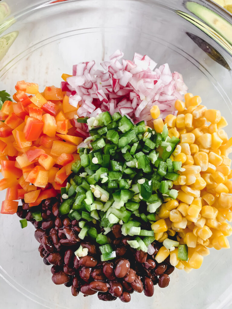 Fiesta salad ingredients chopped up and arranged by color in a glass mixing bowl