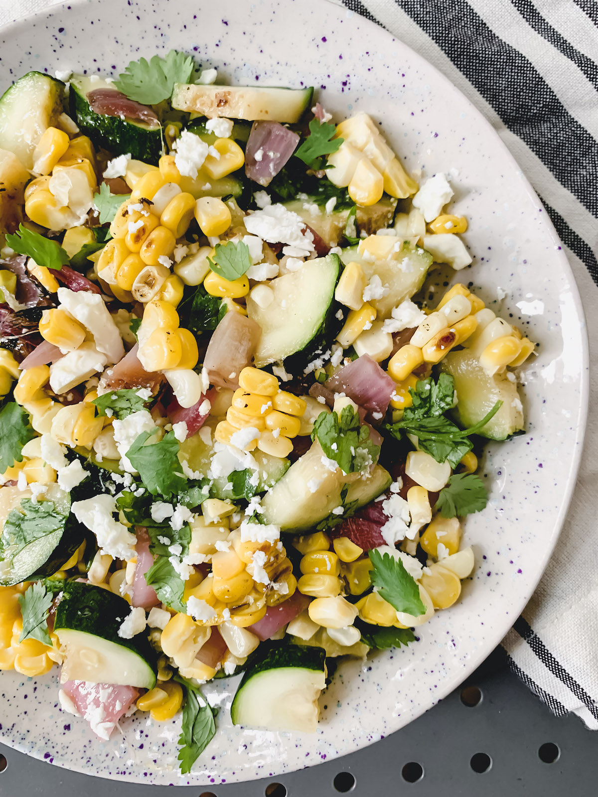 Grilled Corn and Zucchini salad in a speckled bowl with a navy and white striped napkin in the background