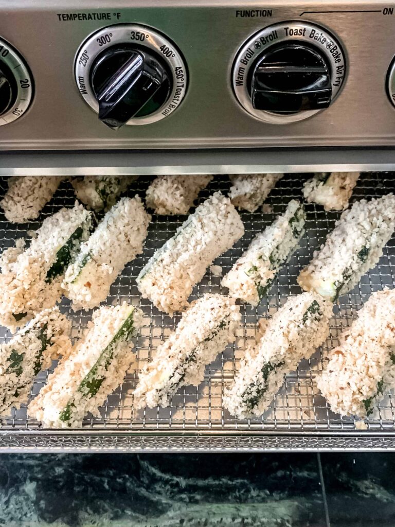 Breaded zucchini fries going into the air fryer oven.