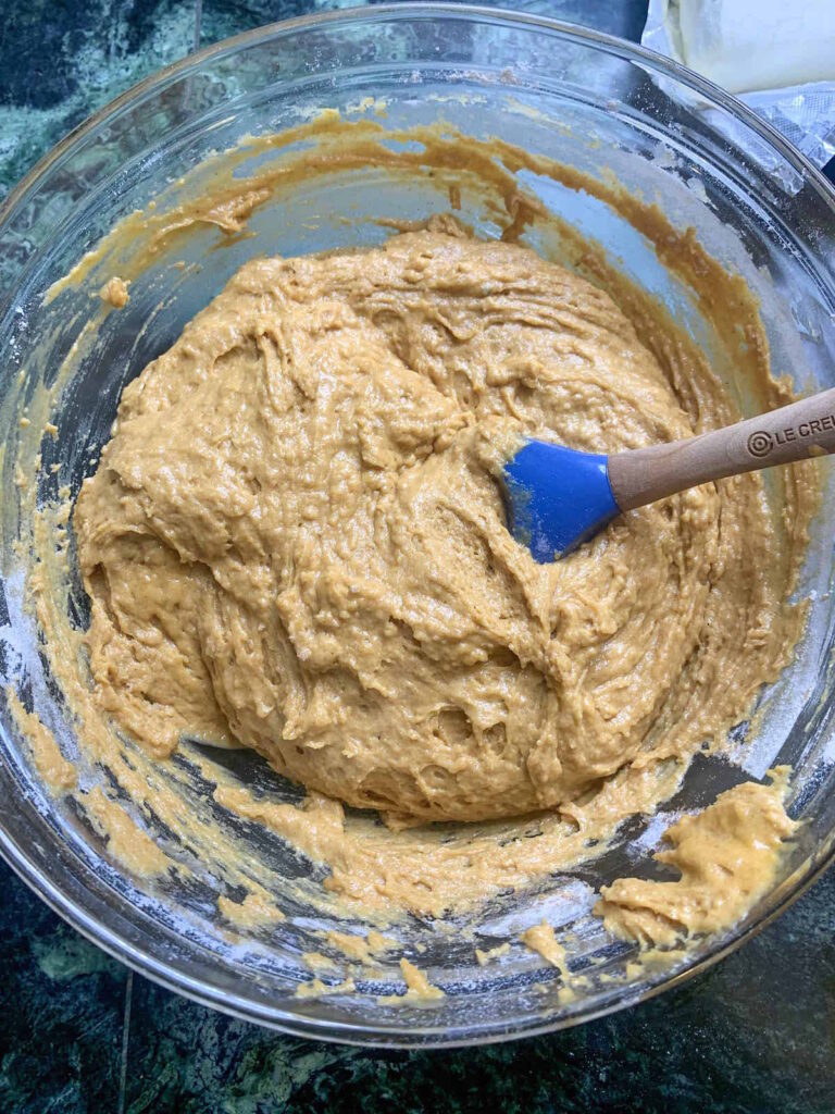 Spiced pumpkin muffin batter in a glass bowl with a blue spatula.