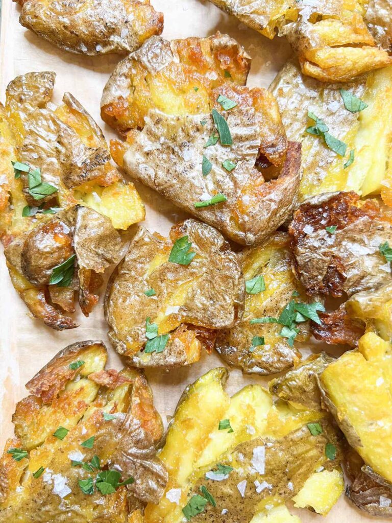 Crispy smashed fingerling potatoes topped with chopped parsley on parchment paper.