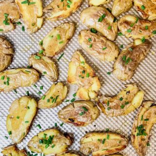 Crispy smashed fingerling potatoes sprinkled with chives on a copper baking sheet.