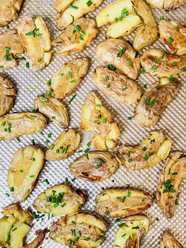 Crispy smashed fingerling potatoes sprinkled with chives on a copper baking sheet.