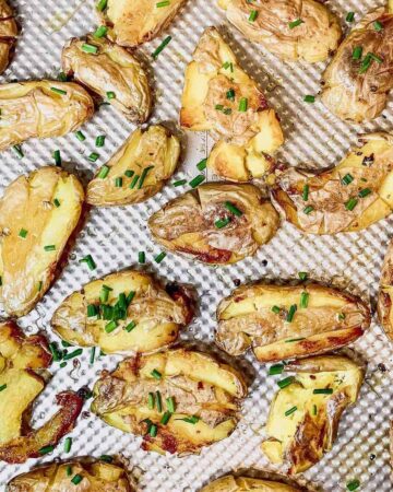 Crispy smashed fingerling potatoes garnished with fresh herbs on a baking sheet.