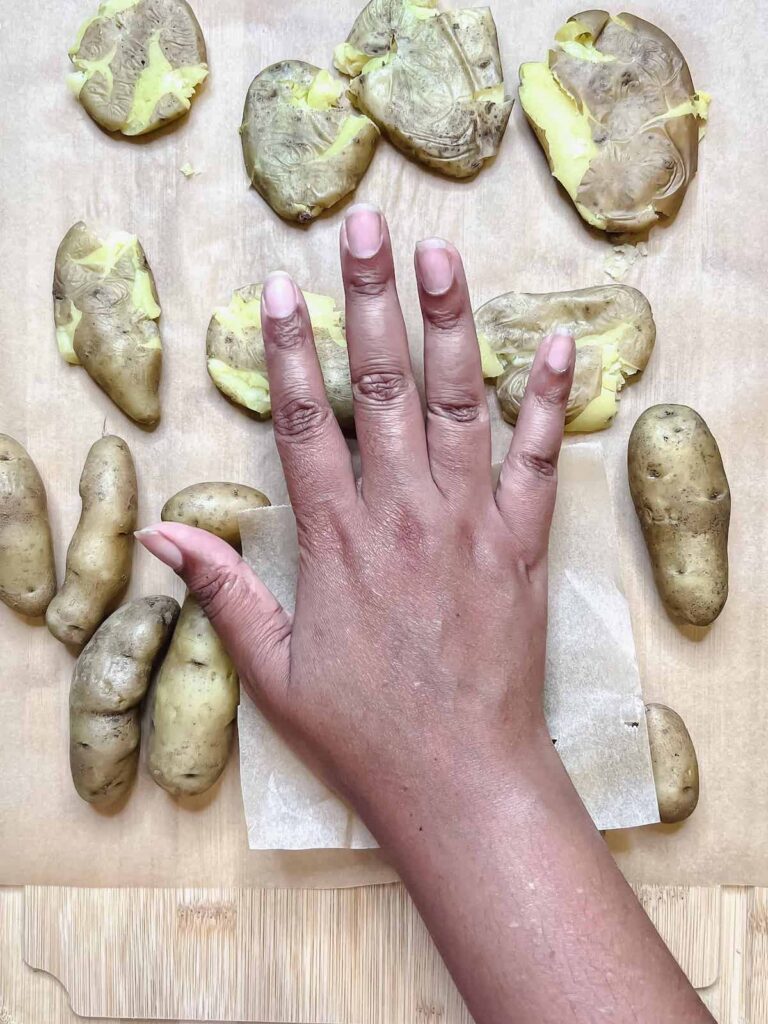 Brown hand smashing fingerling potatoes with parchment paper.