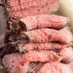 Close up of slices of eye of round roast beef on brown parchment paper.