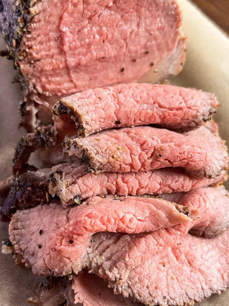 Close up of slices of eye of round roast beef on brown parchment paper.