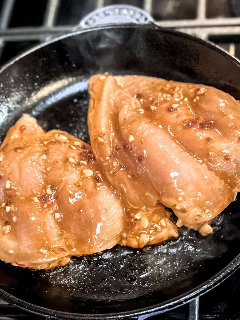 Raw marinated chicken breasts cooking in a cast iron skillet.