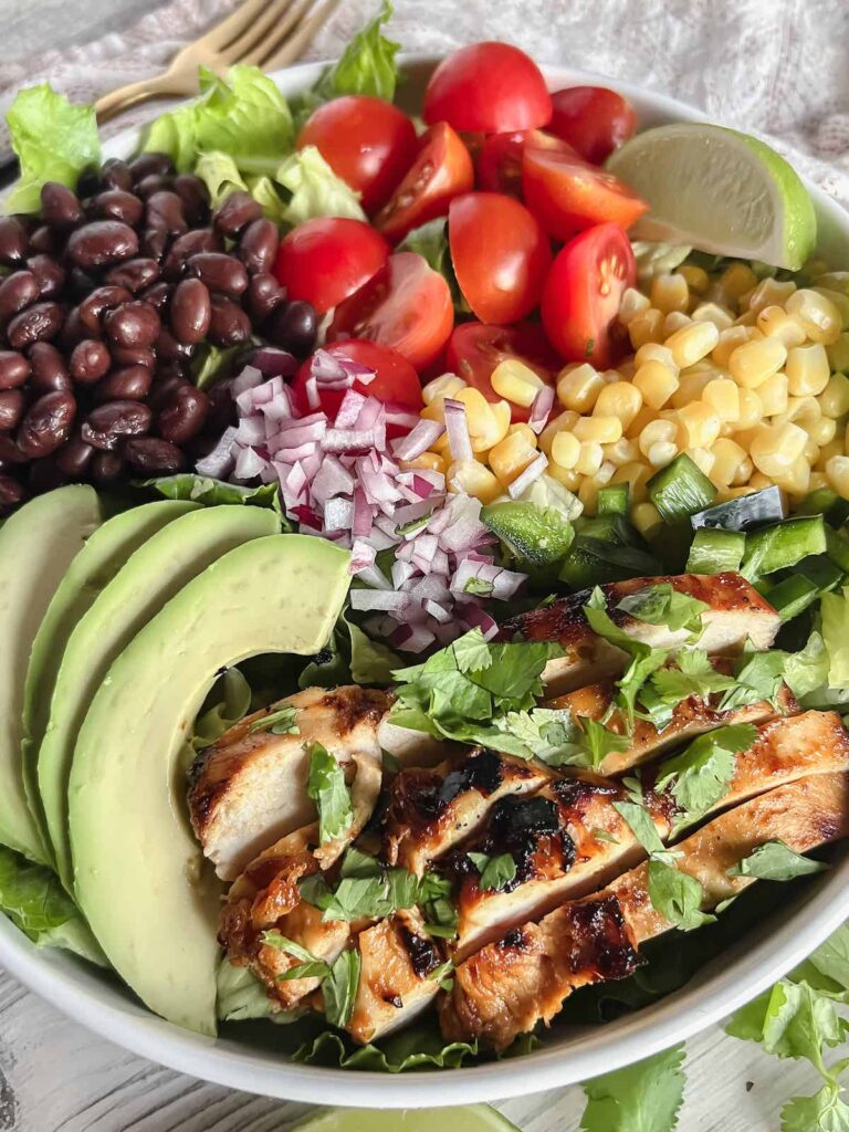 Close up of Southwest Salad with Honey Chipotle Chicken. Ingredients arranged in groupings in a white bowl.