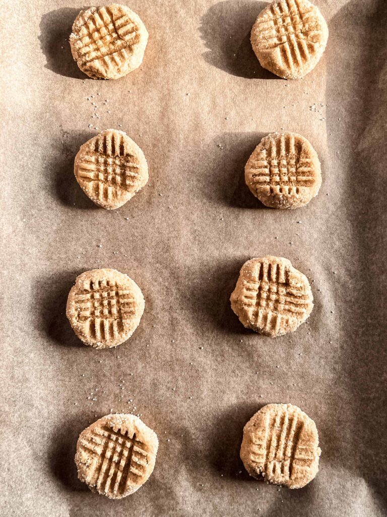Unbaked peanut butter cookies with a criss cross hash mark on a baking sheet lined with parchment paper.