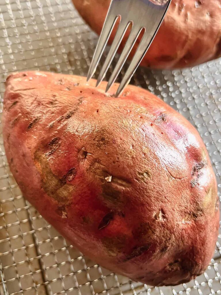 Whole raw sweet potato in air fryer basked being pricked with a fork.