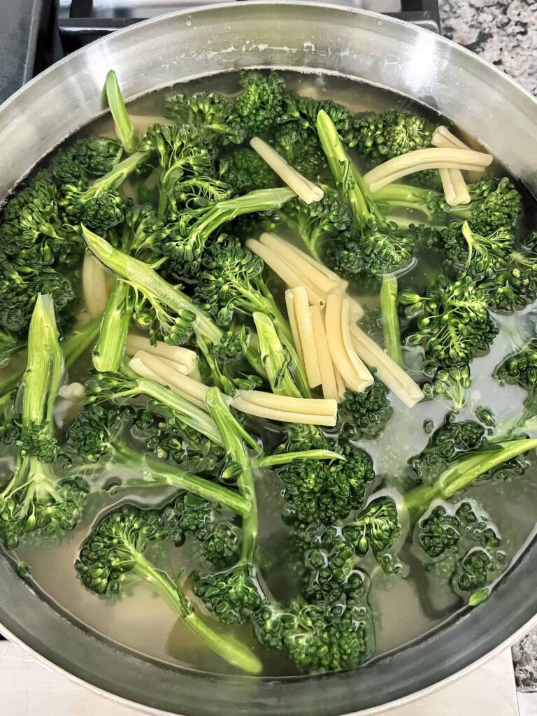 Casarecce pasta and broccolini cooking in pasta water in a stainless steel pot.