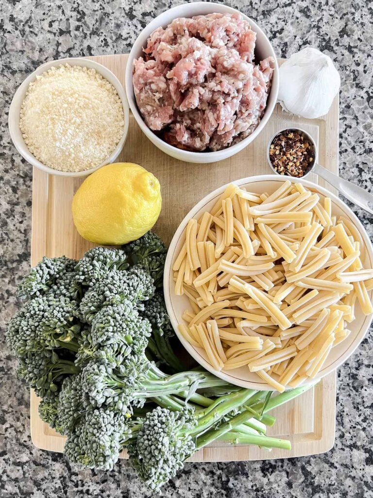 Ingredients for casarecce pasta with broccolini and Italian sausage on a wood cutting board on a granite counter top.