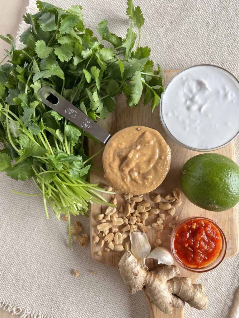 Ingredients for peanut dipping sauce on a small wood cutting board with a bunch of cilantro on the side.
