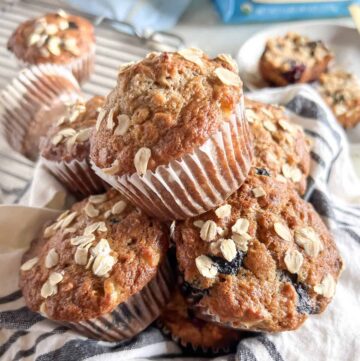 Blueberry banana oatmeal muffins piled in a bowl lined with a blue and white napkin.