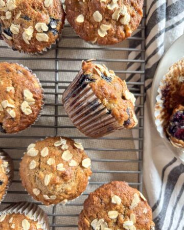 Blueberry banana oatmeal muffin tilted on it's side on top of a cooling rack with more muffins around it.