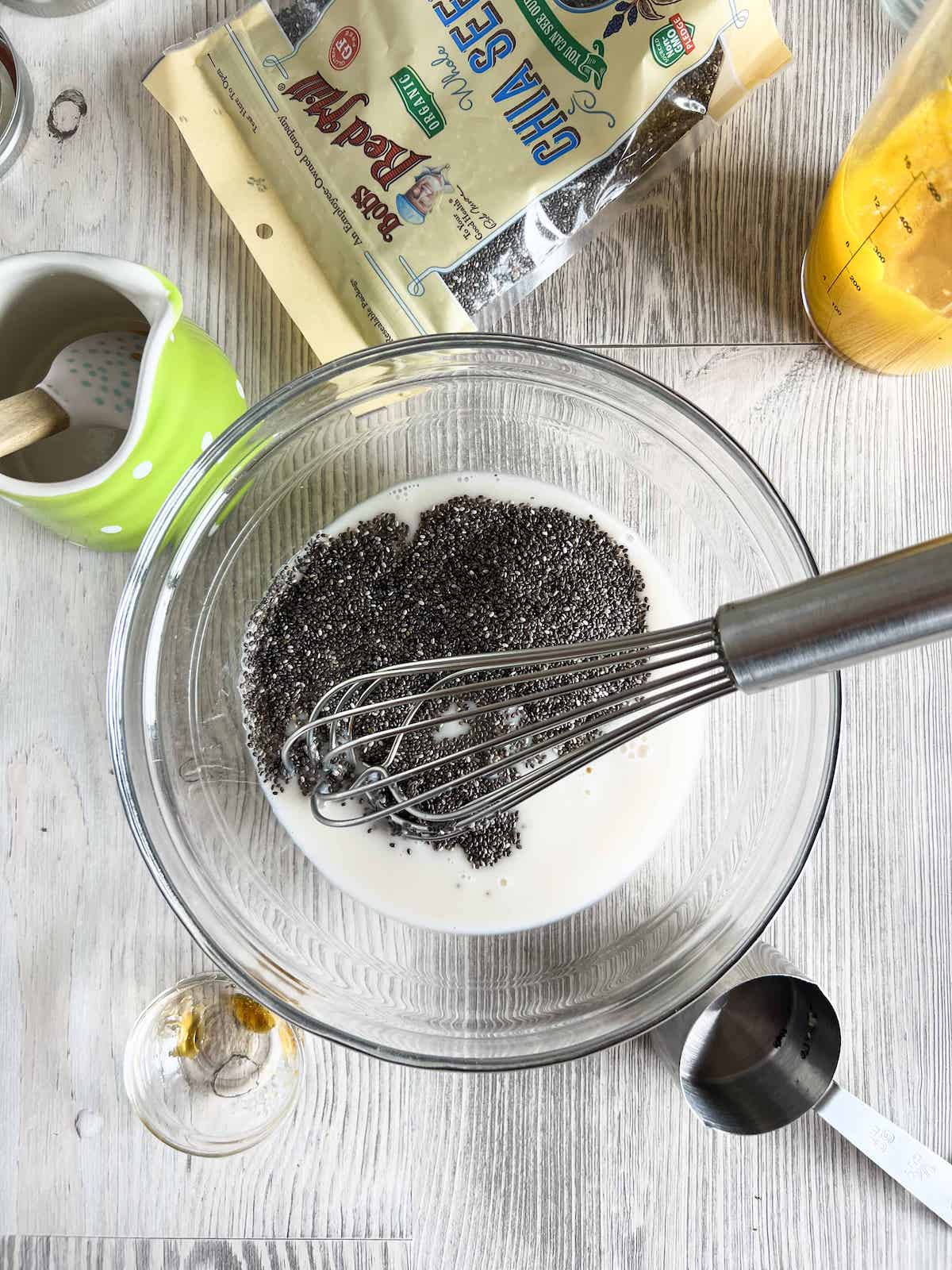 Glass bowl full of almond milk, chia seeds and honey with a metal whisk. 