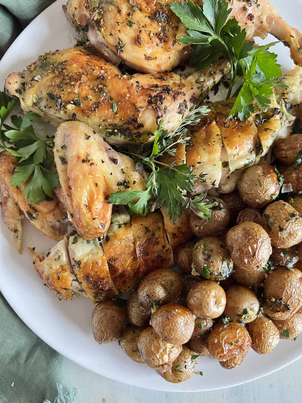 Carved roast chicken with baby potatoes on a white platter with herbs.
