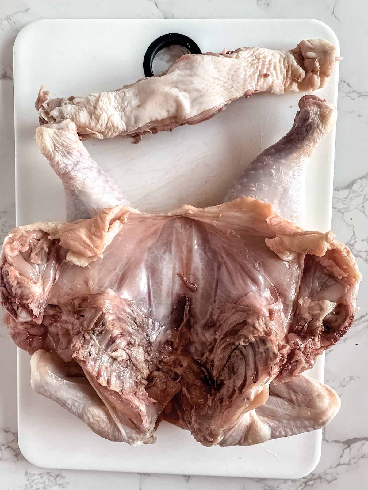 Whole raw chicken with backbone removed.