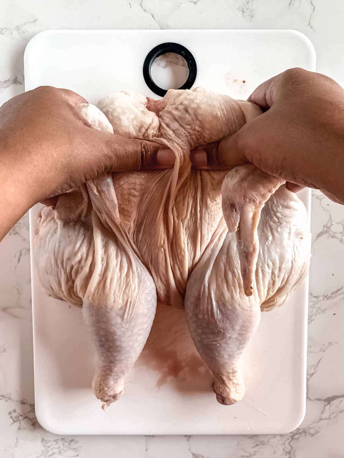 Brown hands breaking breastbone of whole raw chicken.