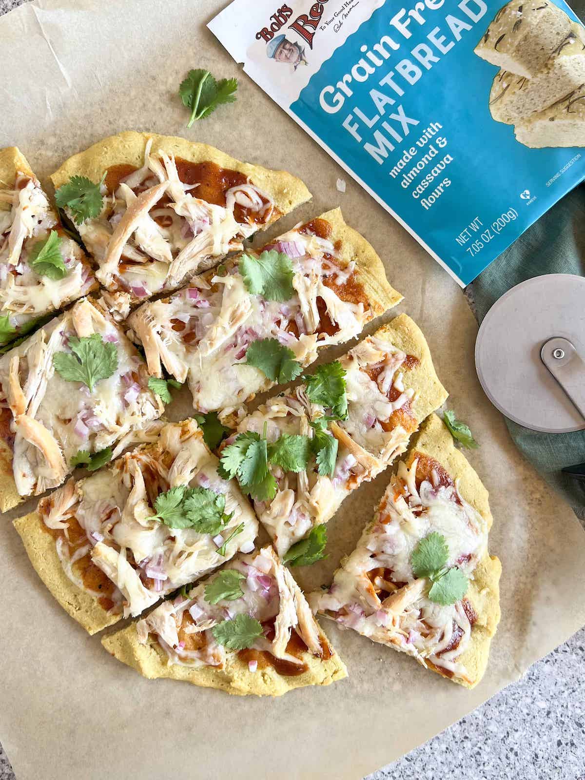 BBQ chicken flatbread pizza cut into pieces next to a pizza cutter and a bag of Bob's Red Mill flatbread mix.