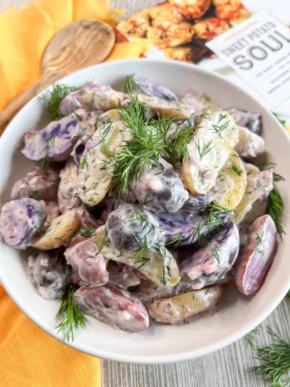 A white bowl full of purple and white potato salad garnished wish sprigs of fresh dill.